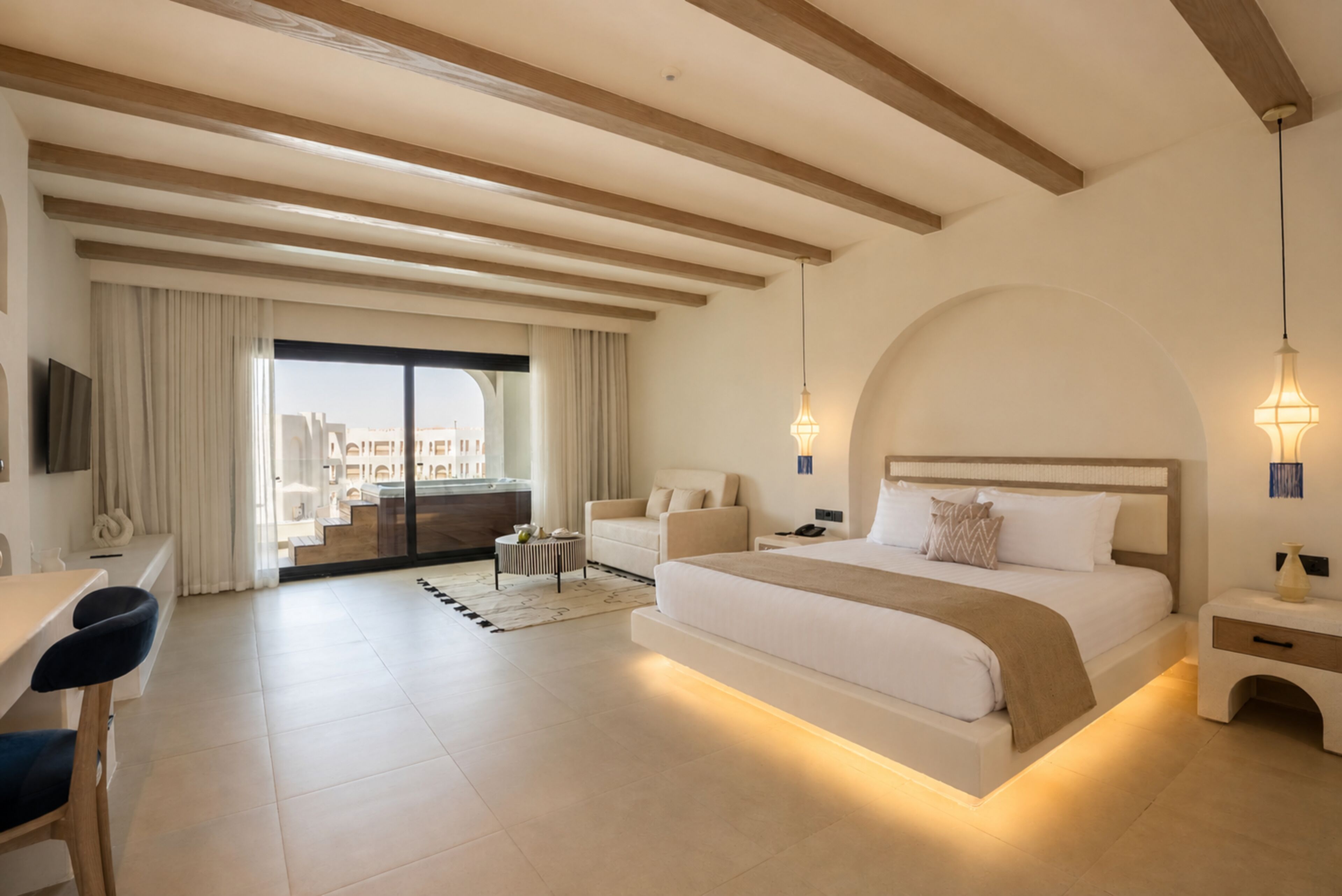 A modern hotel room with a large bed, a desk, a chair, and a balcony with a view.