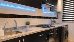 Une cuisine moderne avec des meubles de couleur sombre, un plan de travail en granit, des appareils en acier inoxydable et un éclairage à DEL bleu sous les meubles.