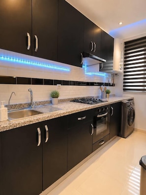 A modern kitchen with dark cabinets, a granite countertop, stainless steel appliances, and blue LED under-cabinet lighting. - Open-Plan 2BR Agadir Apartment | WiFi & Parking (Agadir)