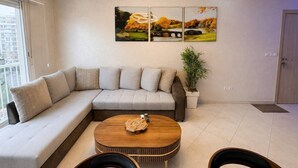 Un salon moderne avec un canapé d’angle, une table basse ronde et un tableau accroché au mur.