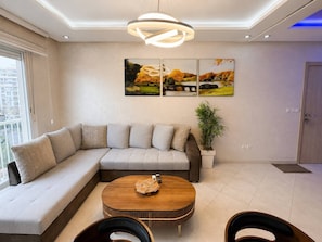 A modern living room with a sectional sofa, a round coffee table, and a wall-mounted painting. - Open-Plan 2BR Agadir Apartment | WiFi & Parking (Agadir)