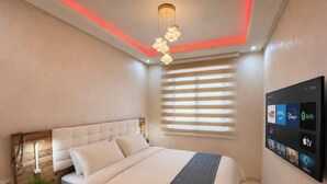 Une chambre à coucher moderne, avec un lit, des tables de chevet, un téléviseur fixé au mur et un luminaire au plafond.