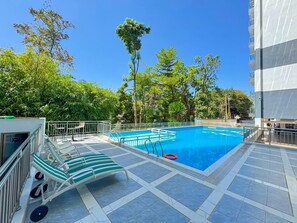 Una piscina con un borde de baldosas, sillas de descanso y un flotador.