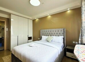 Un dormitorio con una cama grande, un armario, una mesita de noche y una ventana con cortinas.