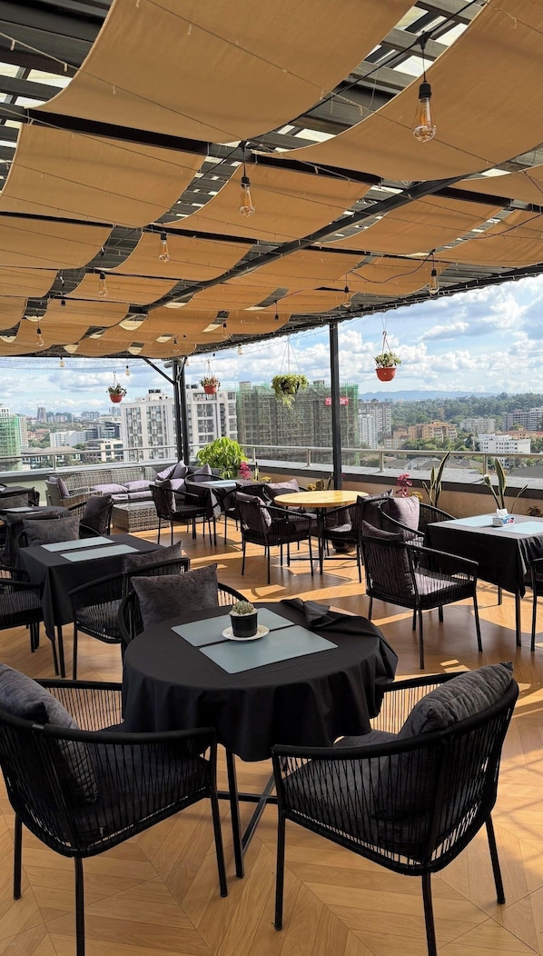 A rooftop restaurant with outdoor seating, tables, chairs, hanging plants, and a city view. - A piece of Heaven (Nairobi)