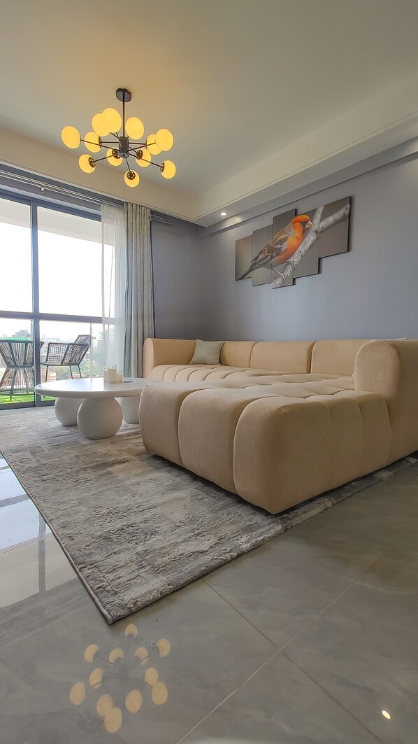 Una sala de estar moderna con un sofá color beige, una mesa de centro redonda y una araña.