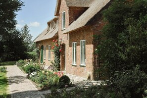 Ein Backsteinhaus mit einem Strohdach, einem Steinweg und einem Garten mit verschiedenen Pflanzen und Blumen.