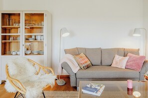 Ein Wohnzimmer mit grauem Sofa, weißem Sessel und einer Vitrine mit Glaswaren.