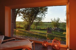 Ein Zimmer mit einem großen Fenster, einem Stuhl mit einem Handtuch und zwei kerzenartigen Objekten auf der Fensterbank.