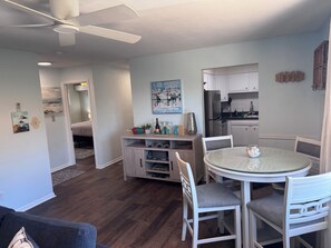 A modern kitchen with white cabinets, a stainless steel refrigerator, and a dining area with a round table and white chairs.