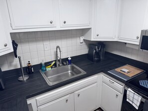 Eine Küche mit weißen Schränken, einer Edelstahlspüle, einer Kaffeemaschine und einem Schneidebrett.