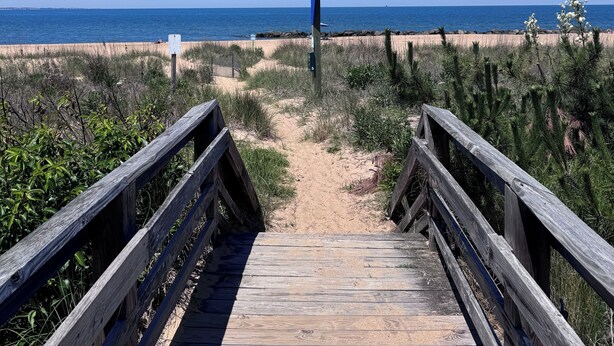 En træpromenade der fører ned til en strand med en klar blå himmel.