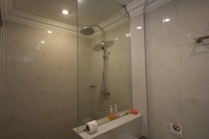 A glass-enclosed shower with a handheld showerhead, a handheld showerhead, and a wall-mounted faucet.