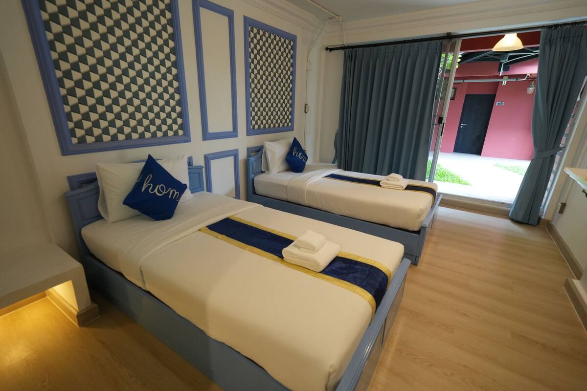 A hotel room with two beds, a patterned wall, and a view of the outside.
