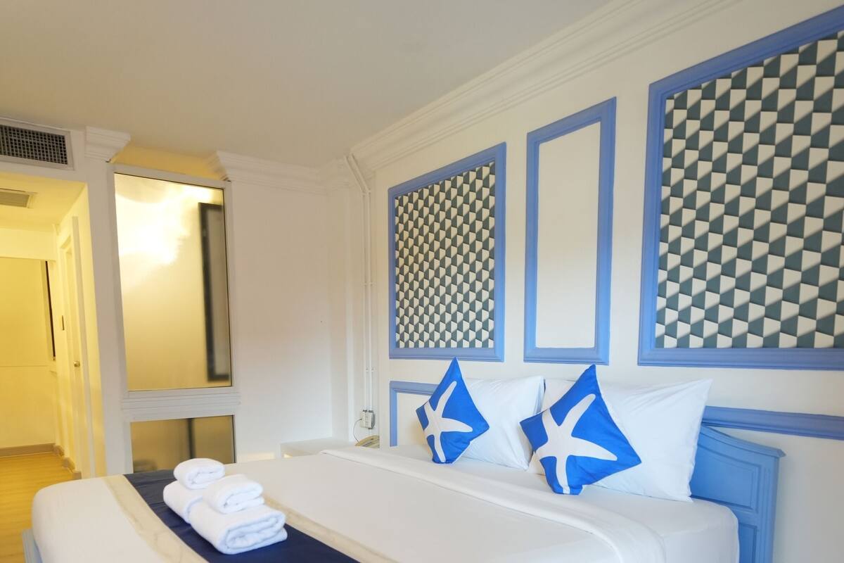A bed with white bedding, blue headboard, and decorative pillows.