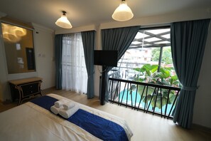 Habitación de hotel con cama, televisión, balcón con vistas a la piscina y ventana con cortinas.