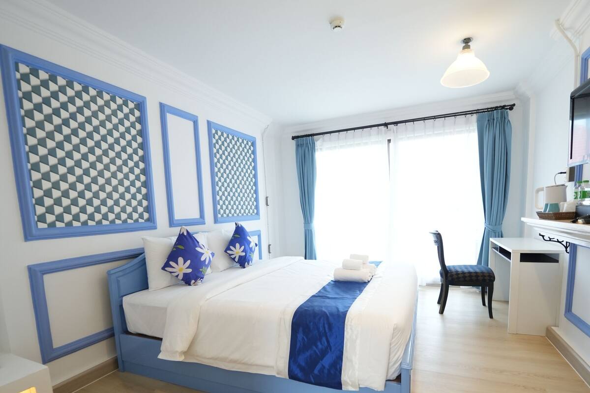 A hotel room with a bed, desk, chair, and large windows.