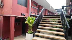 Una escalera con barandilla de metal, una planta en maceta y un edificio con paredes rojas y letreros numerados.