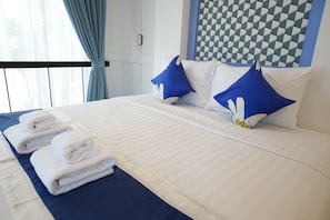A neatly made bed with blue and white pillows, a blue bedspread, and two rolled towels on the side.