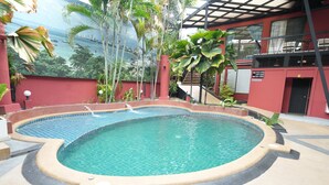 Una piscina con borde de azulejos, rodeada por un edificio rojo con balcón y vista al océano.