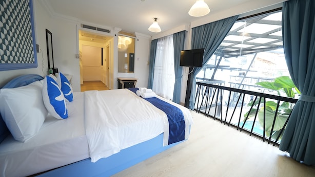 Habitación de hotel con cama, televisión, balcón con barandilla y vistas al exterior.