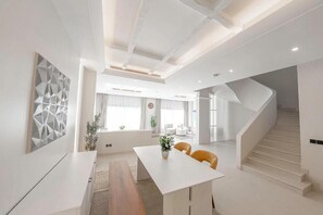 A modern interior with a white dining area, a staircase, and a geometric wall art piece.