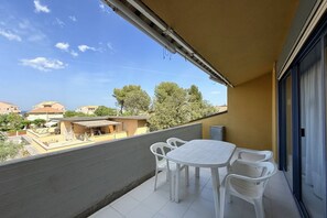 Un balcon avec une table et des chaises, une vue sur les bâtiments et les arbres, et un ciel dégagé.