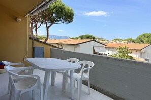 Un balcon avec une table et des chaises, une vue sur des maisons et un arbre.