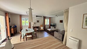 Ein Wohnzimmer mit Sofa, Fernseher, Esstisch und Stühlen.