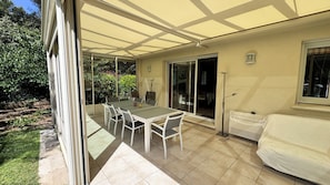 Eine überdachte Terrasse mit Tisch und Stühlen, einer Glasschiebetür und einem weißen Sofa.
