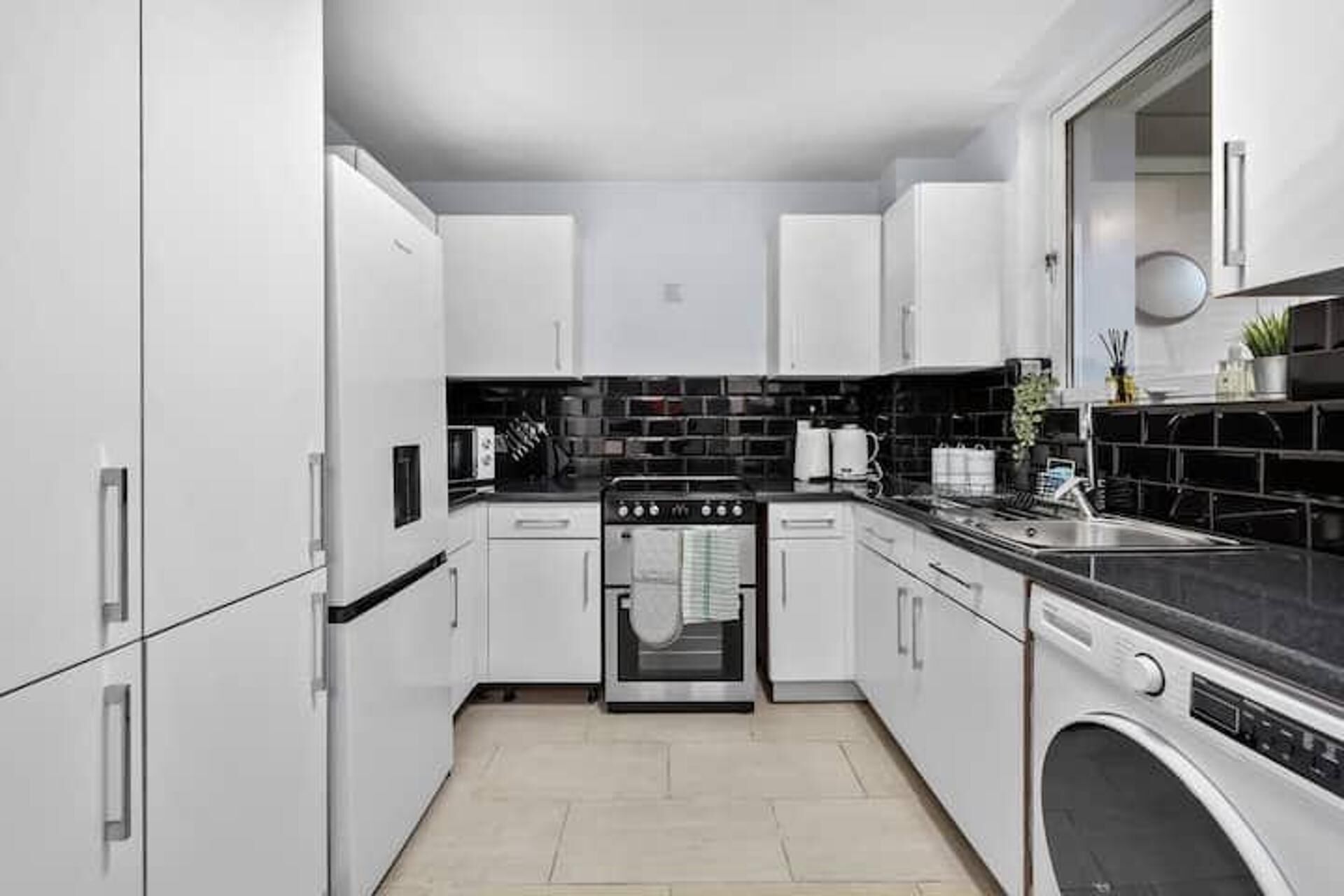 A compact kitchen with white cabinets, a black tiled backsplash, a stainless steel oven, and a built-in dishwasher.