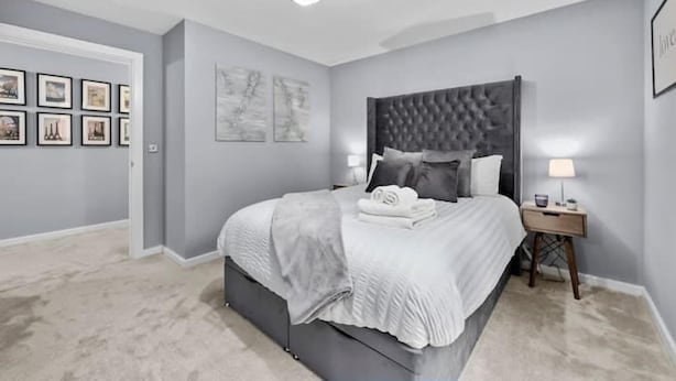 Een slaapkamer met een groot bed, een nachtkastje, een plafondlamp en ingelijste foto's aan de muur.