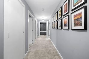 A hallway with framed pictures on the wall, carpeted floor, and white walls. - 1 Bed Apartment Sleeps 3 With Balcony (London)