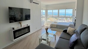 Una sala de estar moderna con televisor de pantalla plana, una mesa de centro de vidrio, un sofá y un ventanal con vistas a la ciudad.