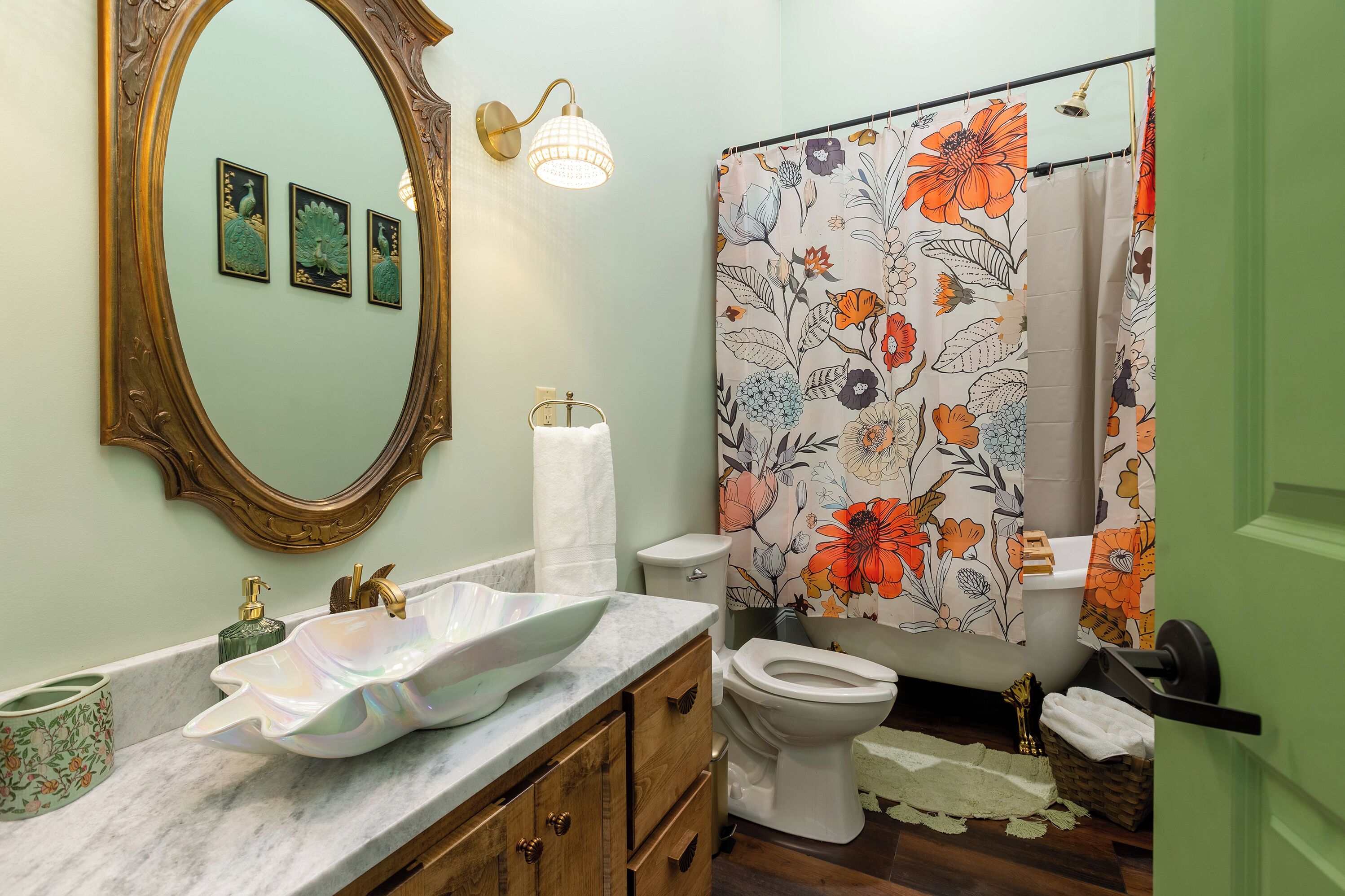 Ein Badezimmer mit Marmor-Waschtisch, Toilette, einer Duschkabine mit Blumenmuster und einem an der Wand befestigten Spiegel.