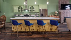 Eine Küche mit grünen Schränken, einem Edelstahl-Kühlschrank und einer Bar mit blauen Stühlen.