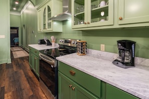 A kitchen with green cabinets, a stove, a coffee maker, and a microwave.