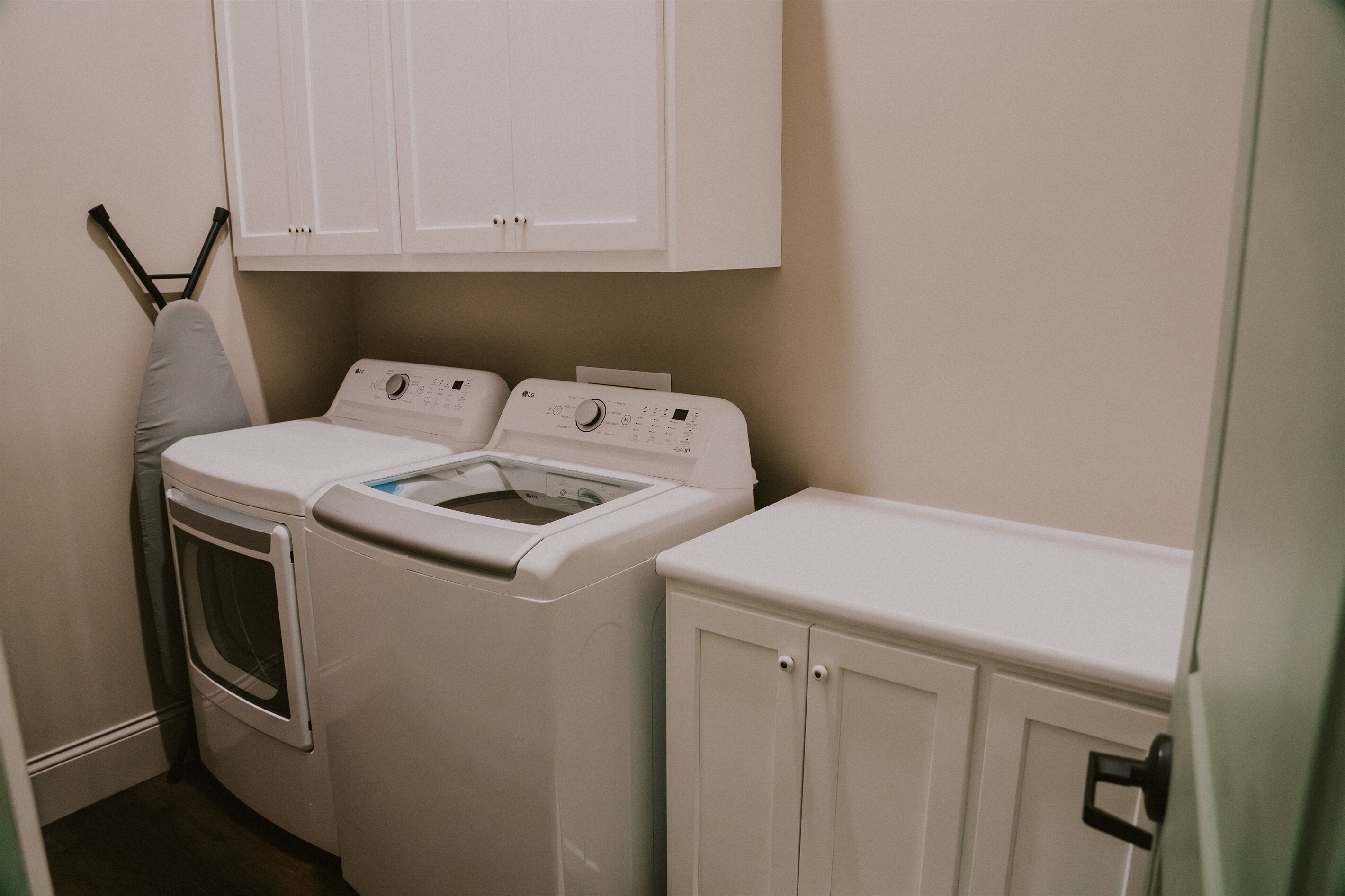 Een wasserette met een wasmachine en droger, een droogrek en witte kasten.