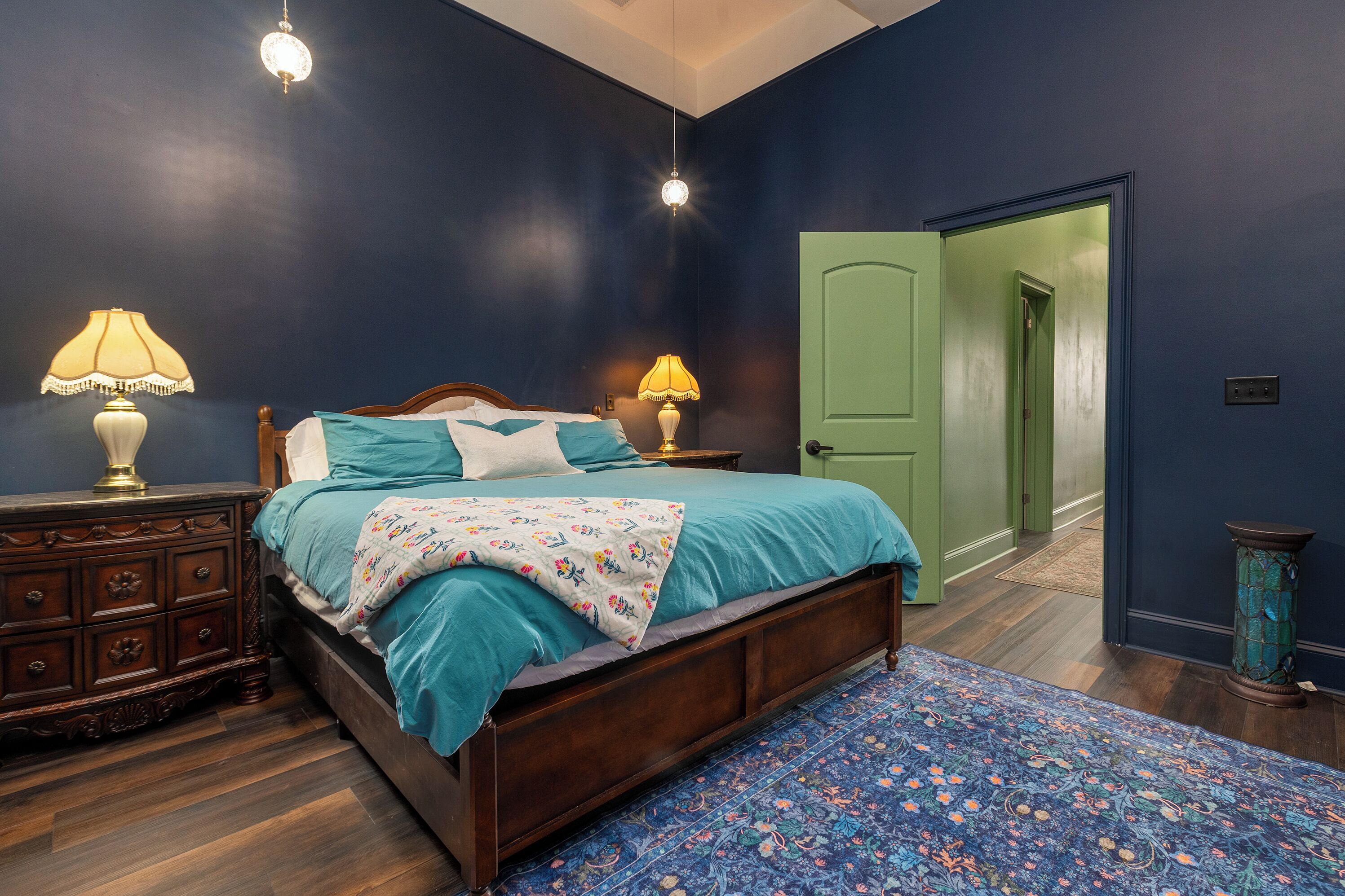 Een slaapkamer met een houten bed, twee bedlampen, een groene deur en een kamerbreed tapijt met een patroon.