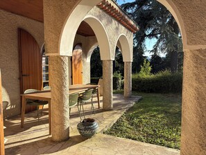 A covered patio with a table and chairs, a potted plant, and an arched architectural feature. - Los Arcos | Two renovated houses for 15 people. 4-legged friends too! (Annonay)