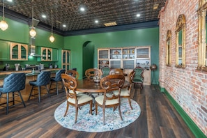 A dining area with a round table, six chairs, a patterned rug, and a brick wall.