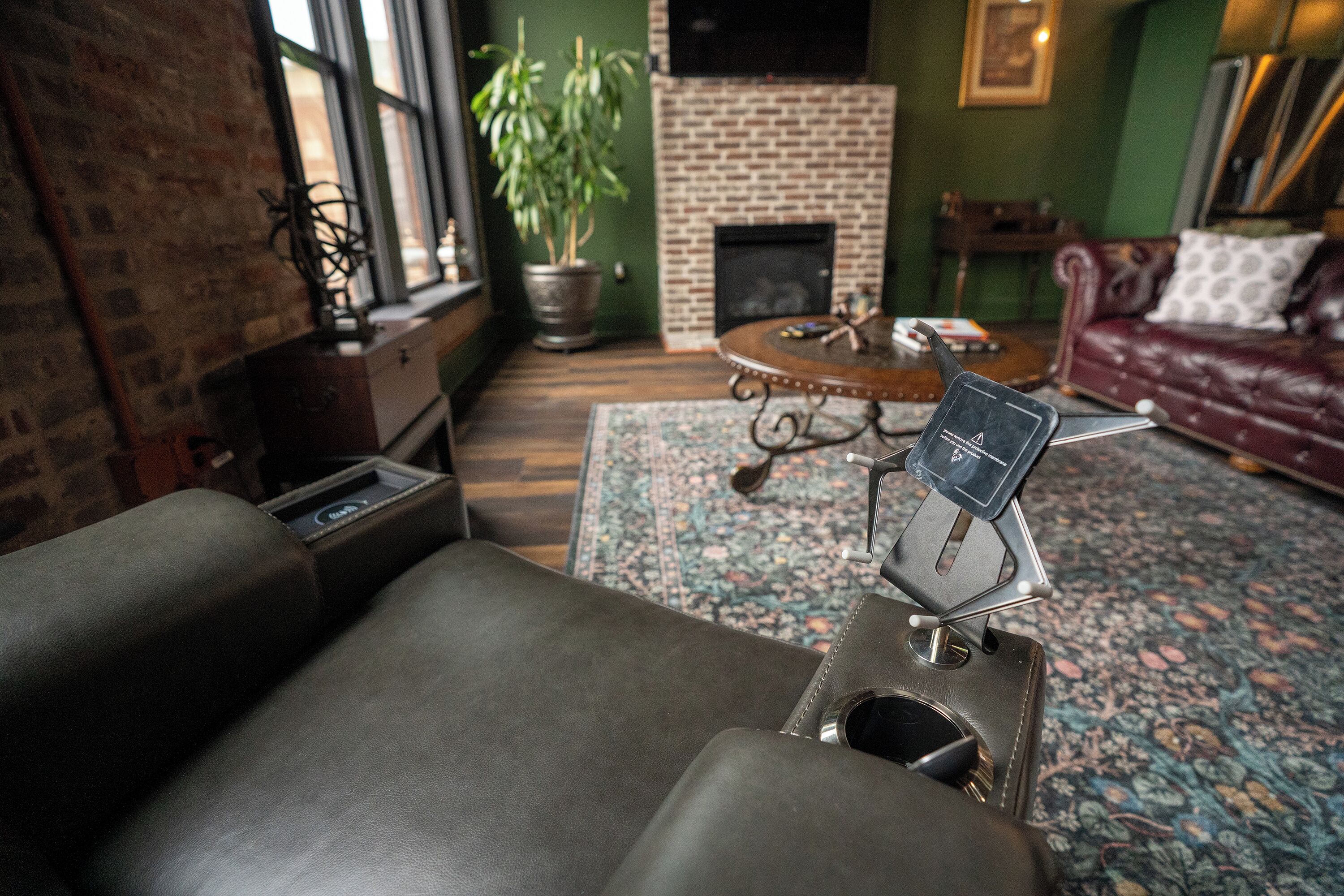 A living room with a leather sofa, a fireplace, a TV mounted on the wall, and a potted plant.