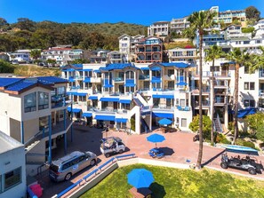 Un hotel de varios pisos con balcones, un estacionamiento y vistas a una colina.