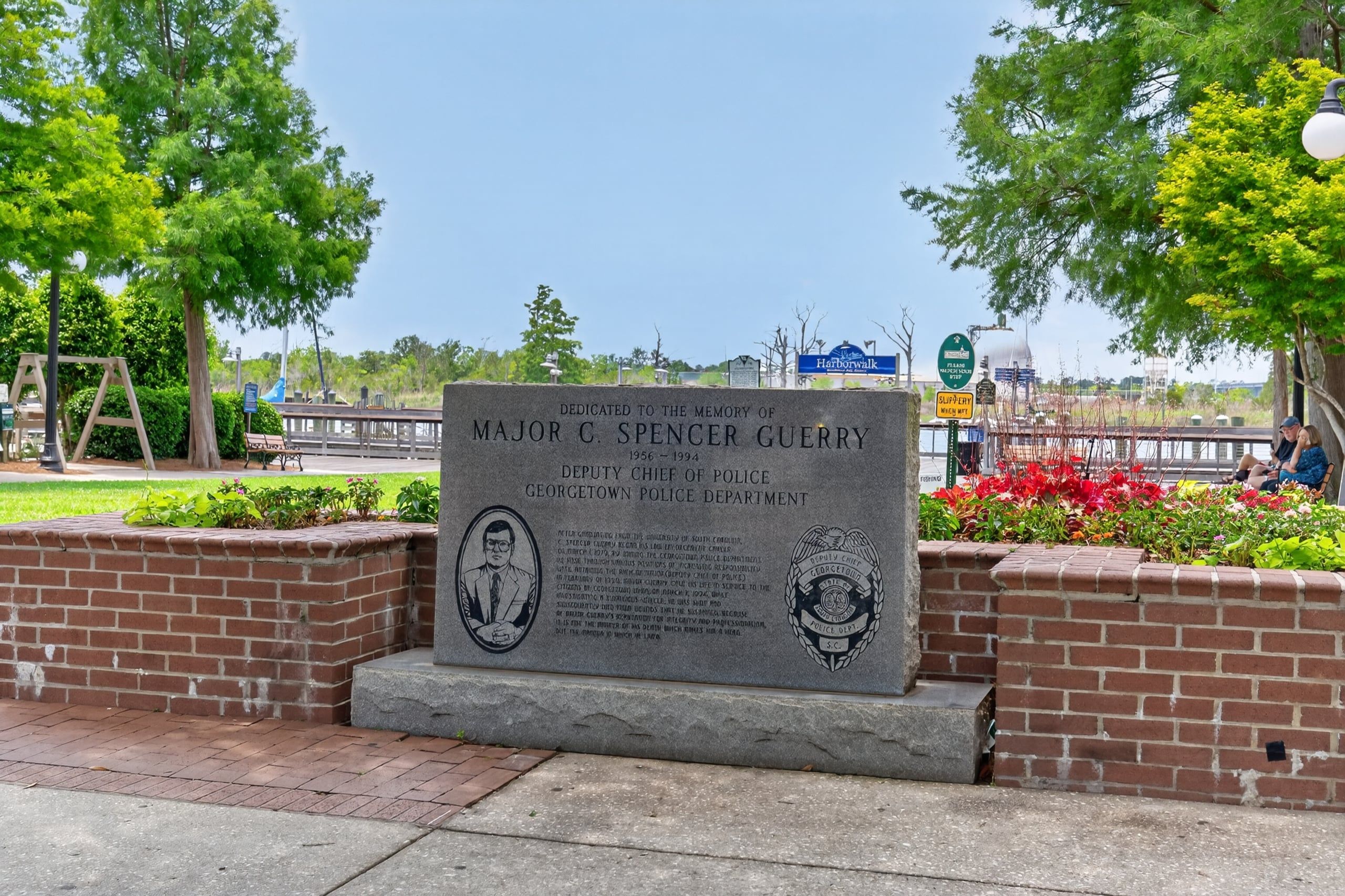 Placa comemorativa dedicada ao Major C. Spencer Guerry, Chefe de Polícia Adjunto, com vista para um parque e uma ponte ao fundo.