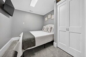 A bedroom with a bed, a wardrobe, a flat-screen TV mounted on the wall, and a ceiling light.