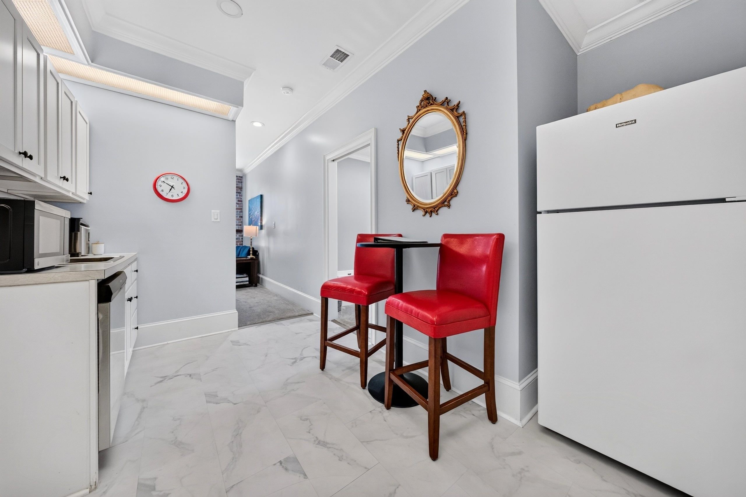 A modern kitchen with white cabinetry, a red-framed mirror, and a white refrigerator.