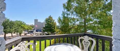 En balkon med et rundt bord og to stole, med udsigt over en parkeringsplads og en bygning med et flagstang.
