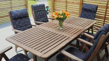 Una mesa de madera con cuatro sillas, un jarrón con flores y una valla de madera al fondo.