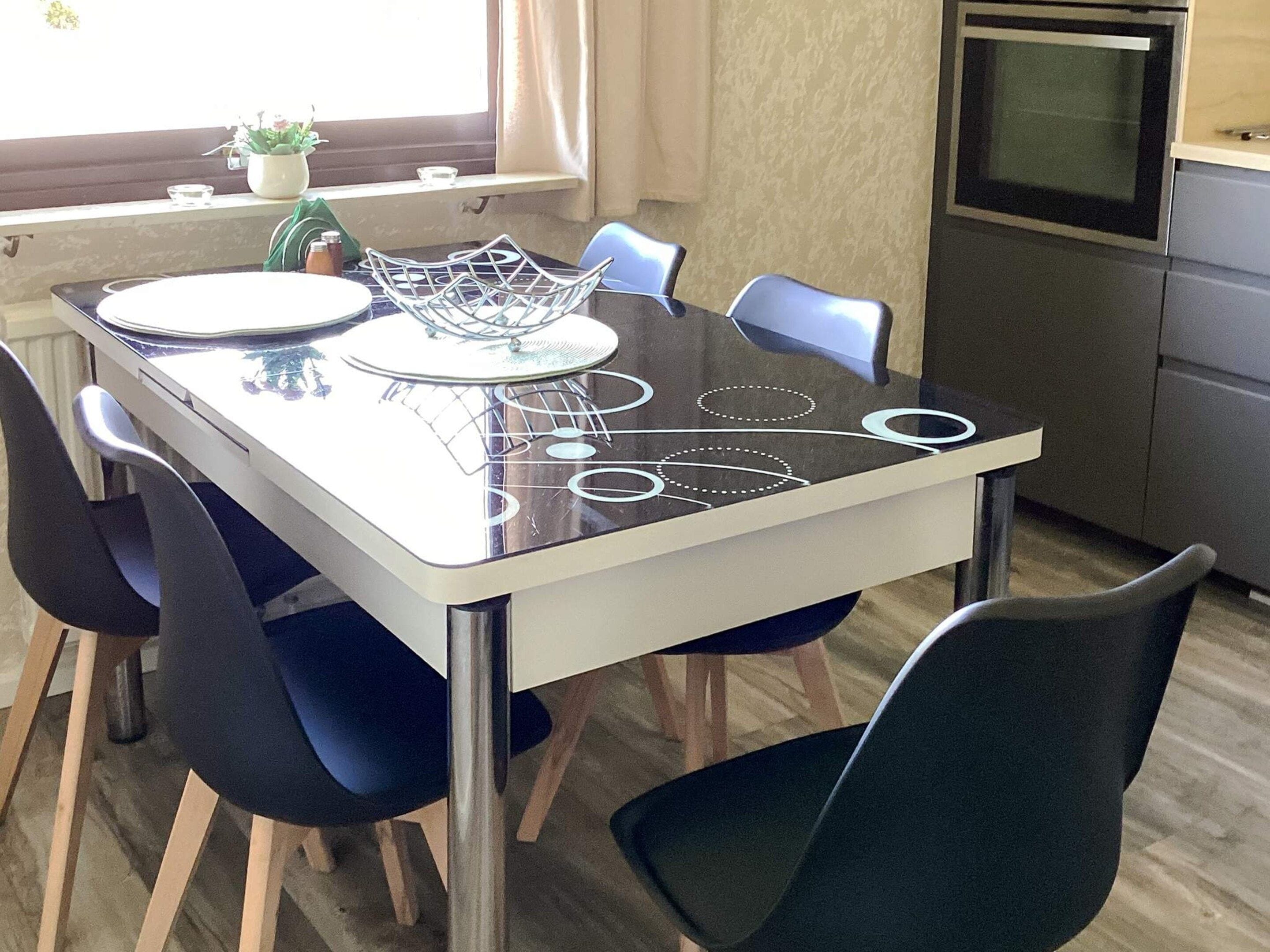 Una mesa de comedor con diseño moderno, rodeada de sillas, en una habitación con ventana y zona de cocina.
