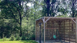 Una pérgola de madera con un columpio en un área cubierta de césped, rodeada de árboles.